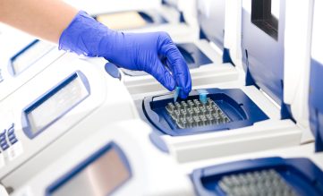 en hand som sätter ner ett litet provrör i en pcr-maskin